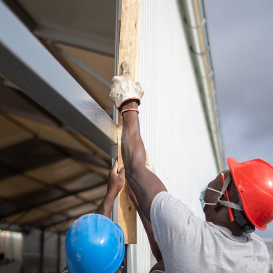 afro-american-builders-wearing-helmets-face-masks-while-measuring-wall_181624-58281